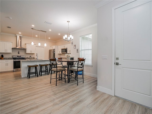 dining space featuring sink, crown molding, a notable chandelier, and light wood-type flooring