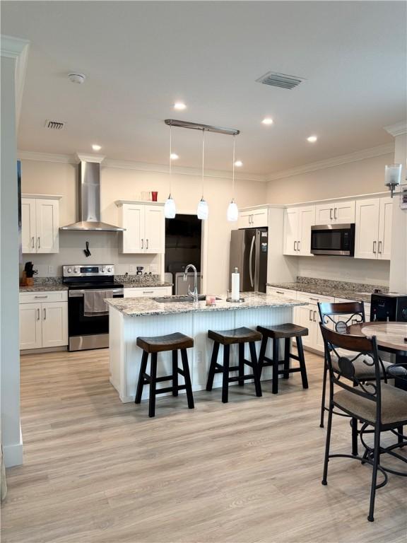 kitchen featuring stainless steel appliances, white cabinetry, light stone counters, and wall chimney exhaust hood