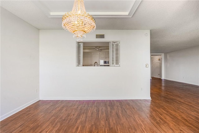 empty room featuring a chandelier, wood finished floors, baseboards, and a textured ceiling