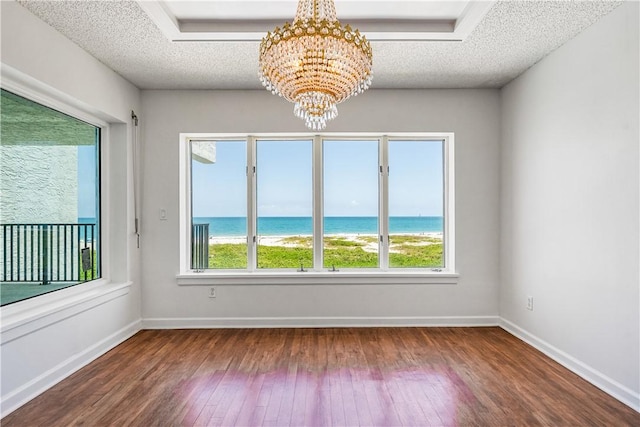 empty room featuring wood-type flooring, a chandelier, a textured ceiling, a water view, and baseboards