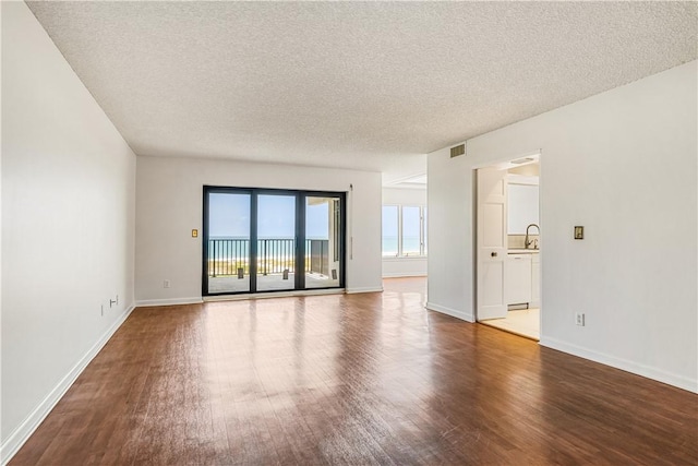 unfurnished room with a textured ceiling, dark wood-style flooring, baseboards, and a sink