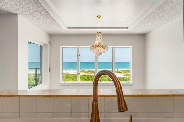 kitchen view of a chandelier, a water view, a raised ceiling, decorative light fixtures, and a textured ceiling