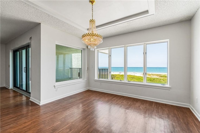 unfurnished room featuring a chandelier, dark wood-style flooring, a water view, baseboards, and a textured ceiling