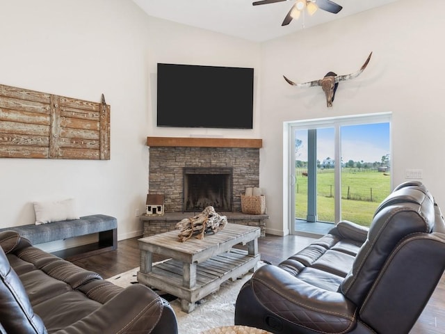 living room with wood-type flooring, a stone fireplace, and ceiling fan