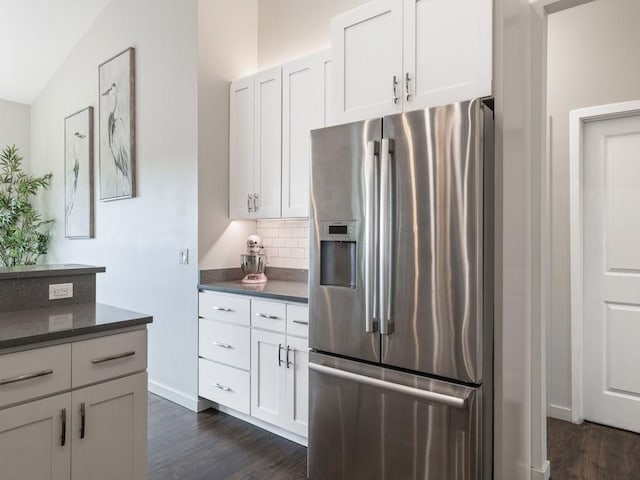 kitchen with stainless steel refrigerator with ice dispenser, dark hardwood / wood-style floors, vaulted ceiling, and white cabinets