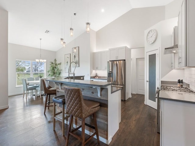 kitchen with appliances with stainless steel finishes, hanging light fixtures, tasteful backsplash, an island with sink, and a kitchen bar