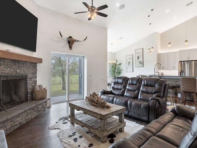 living room with dark wood-type flooring, a stone fireplace, sink, vaulted ceiling, and ceiling fan