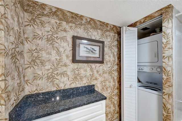 clothes washing area with a textured ceiling and stacked washer / dryer