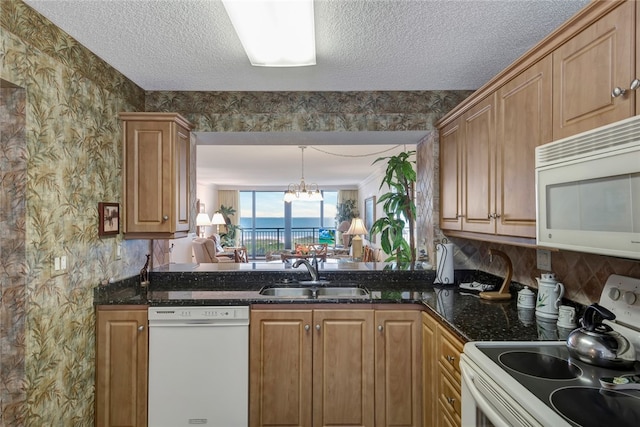 kitchen with white appliances, sink, hanging light fixtures, dark stone countertops, and a notable chandelier