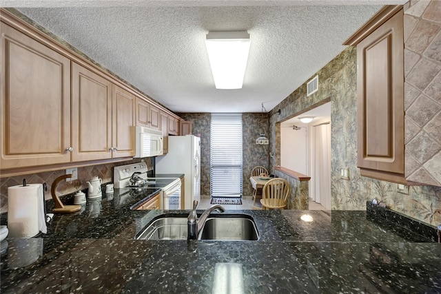 kitchen with a textured ceiling, white appliances, dark stone countertops, and sink