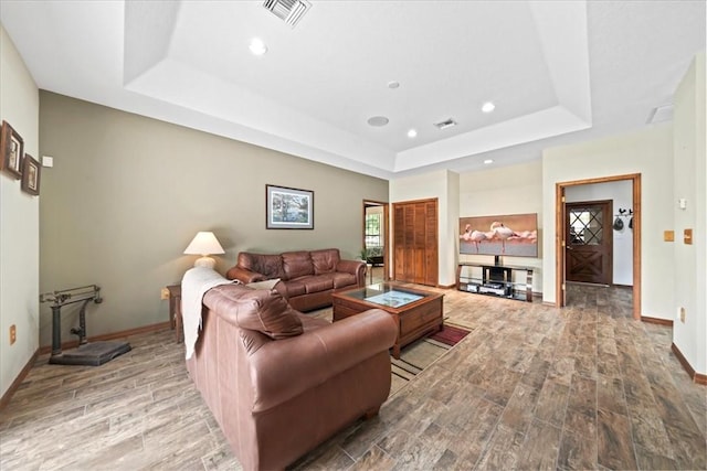 living room with visible vents, baseboards, a raised ceiling, and wood finished floors