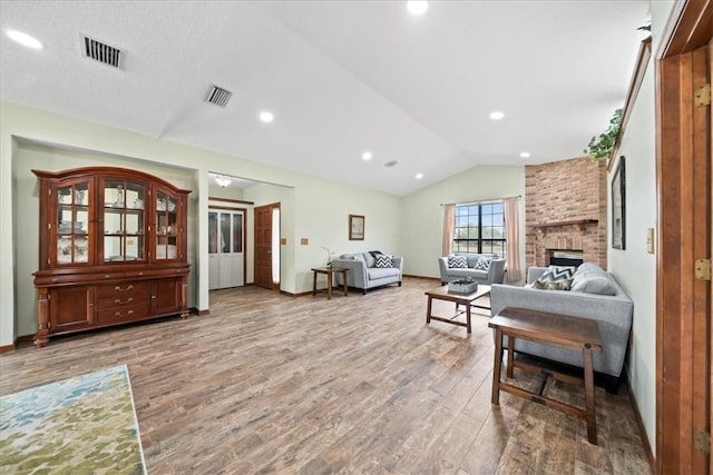 living area with a fireplace, visible vents, vaulted ceiling, and wood finished floors