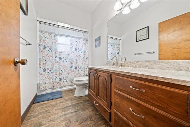 full bath featuring vanity, baseboards, toilet, shower / bath combo with shower curtain, and wood finished floors