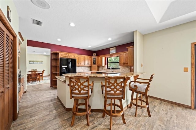 kitchen featuring visible vents, black fridge, a peninsula, light wood-style flooring, and light stone counters