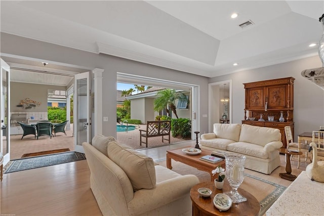 living room with ornate columns, light hardwood / wood-style floors, and a raised ceiling