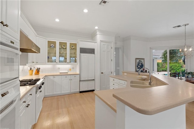 kitchen with range hood, a center island with sink, an inviting chandelier, white cabinetry, and hanging light fixtures