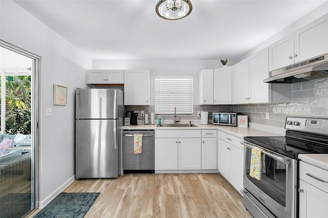 kitchen featuring a sink, light countertops, under cabinet range hood, appliances with stainless steel finishes, and backsplash