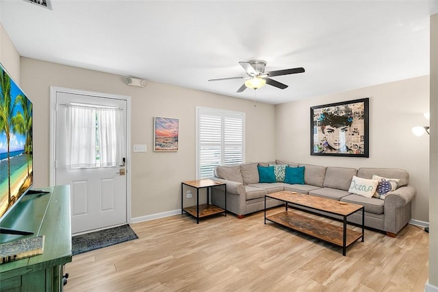 living area featuring a ceiling fan, baseboards, and light wood finished floors