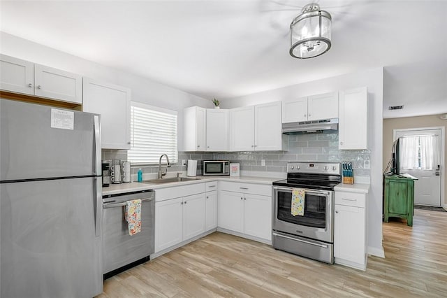 kitchen with tasteful backsplash, under cabinet range hood, light countertops, stainless steel appliances, and a sink