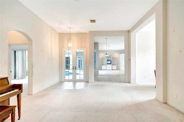 unfurnished room with arched walkways, light carpet, visible vents, baseboards, and french doors