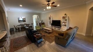 living room featuring wood-type flooring, ceiling fan, and ornamental molding