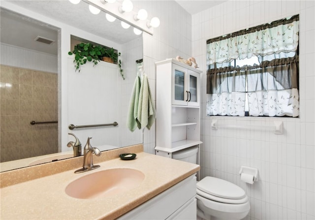 bathroom with vanity, toilet, and tile walls