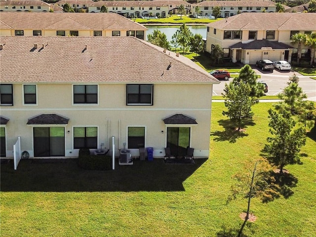 back of property with a lawn, central AC, and a water view