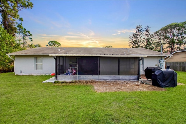 back of property at dusk with a yard, stucco siding, and a sunroom