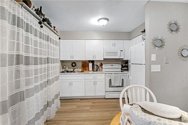 kitchen with white cabinetry, sink, white appliances, and light hardwood / wood-style flooring