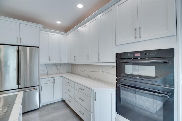 kitchen featuring white cabinetry, black double oven, decorative backsplash, and stainless steel fridge