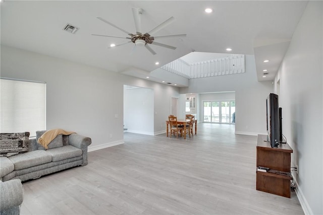 living room featuring ceiling fan, a high ceiling, and light hardwood / wood-style flooring