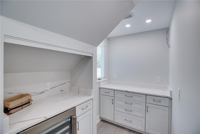 kitchen featuring wine cooler, light stone countertops, and light hardwood / wood-style flooring