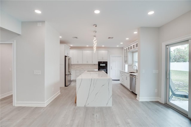 kitchen with white cabinetry, stainless steel appliances, light stone countertops, a kitchen island, and sink