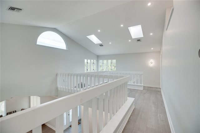 corridor featuring light wood-type flooring, a skylight, and high vaulted ceiling