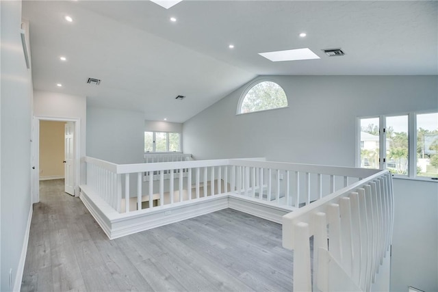 corridor with lofted ceiling with skylight and light hardwood / wood-style flooring