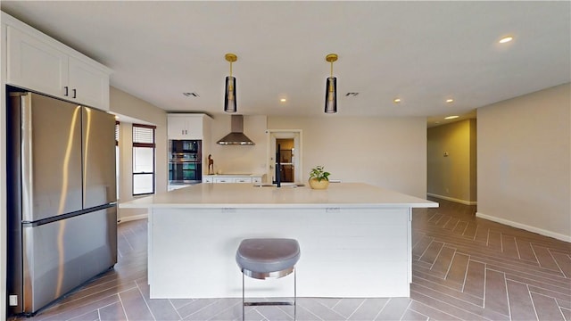 kitchen with white cabinets, stainless steel refrigerator, wall chimney exhaust hood, and an island with sink