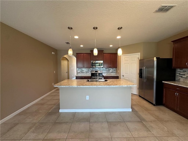 3315 Rockport St SW, Vero Beach, FL 32968 - kitchen with appliances with stainless steel finishes, backsplash, arched walkways, an island with sink, and light tile patterned floors