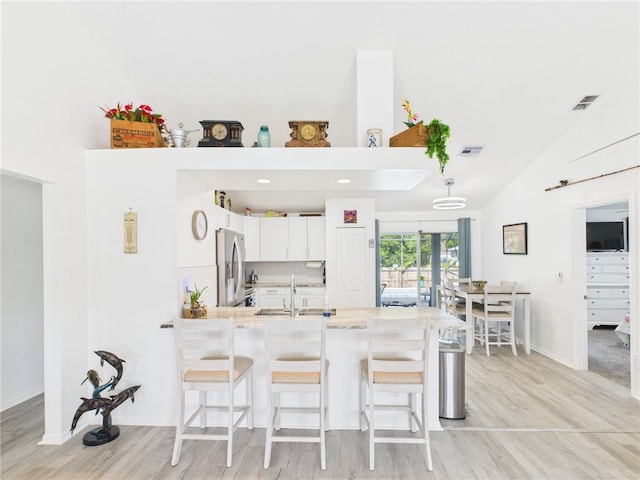 7965 105th Ave, Vero Beach, FL 32967 - kitchen featuring stainless steel refrigerator with ice dispenser, a peninsula, a breakfast bar area, white cabinetry, and high vaulted ceiling