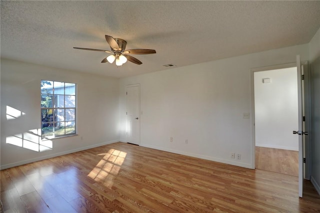 empty room with wood finished floors, a textured ceiling, baseboards, visible vents, and ceiling fan