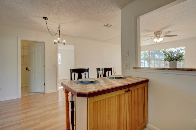 kitchen with a textured ceiling, visible vents, tile countertops, light wood-style floors, and ceiling fan with notable chandelier