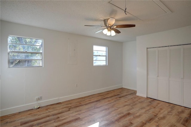 unfurnished bedroom with electric panel, attic access, light wood finished floors, a textured ceiling, and baseboards