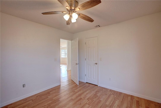spare room featuring a ceiling fan, baseboards, light wood finished floors, and a textured ceiling