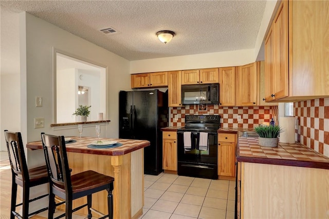 kitchen featuring visible vents, tile counters, a breakfast bar, black appliances, and light tile patterned floors