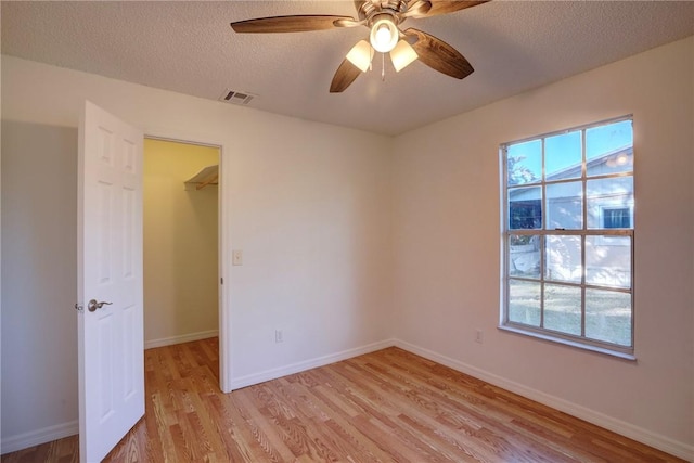 unfurnished bedroom featuring a walk in closet, baseboards, a textured ceiling, light wood finished floors, and visible vents