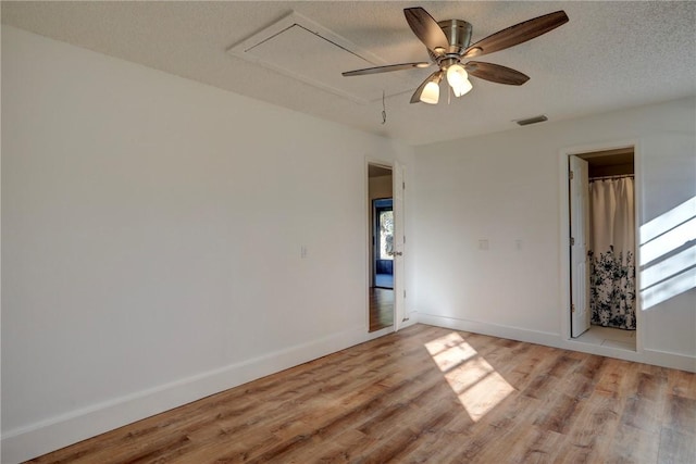 empty room featuring attic access, light wood-type flooring, baseboards, a textured ceiling, and a ceiling fan