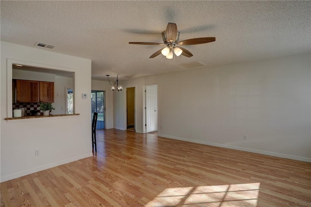 unfurnished living room featuring ceiling fan with notable chandelier, baseboards, a textured ceiling, visible vents, and light wood-style flooring