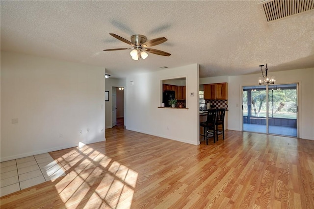 unfurnished living room featuring light wood finished floors, ceiling fan with notable chandelier, visible vents, and a textured ceiling