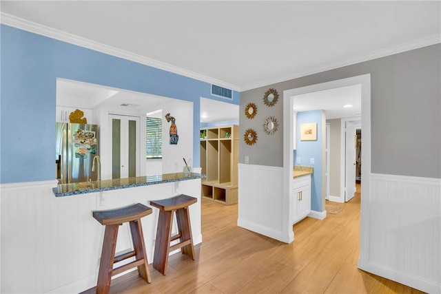 kitchen with a kitchen breakfast bar, stainless steel refrigerator with ice dispenser, dark stone countertops, light wood-type flooring, and white cabinetry