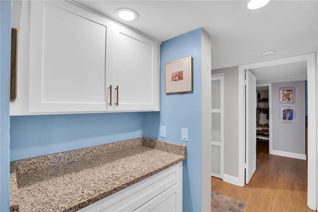 kitchen featuring white cabinets, light stone counters, and light wood-type flooring