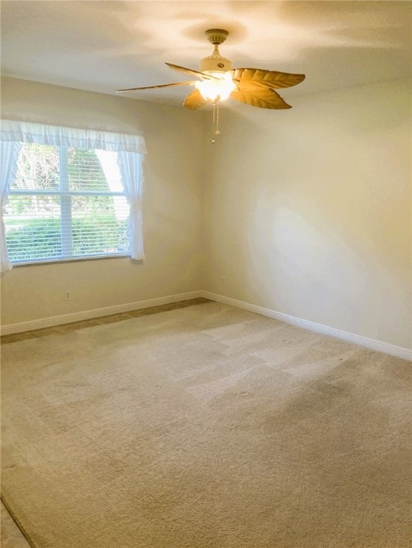 spare room with a ceiling fan, light colored carpet, and baseboards